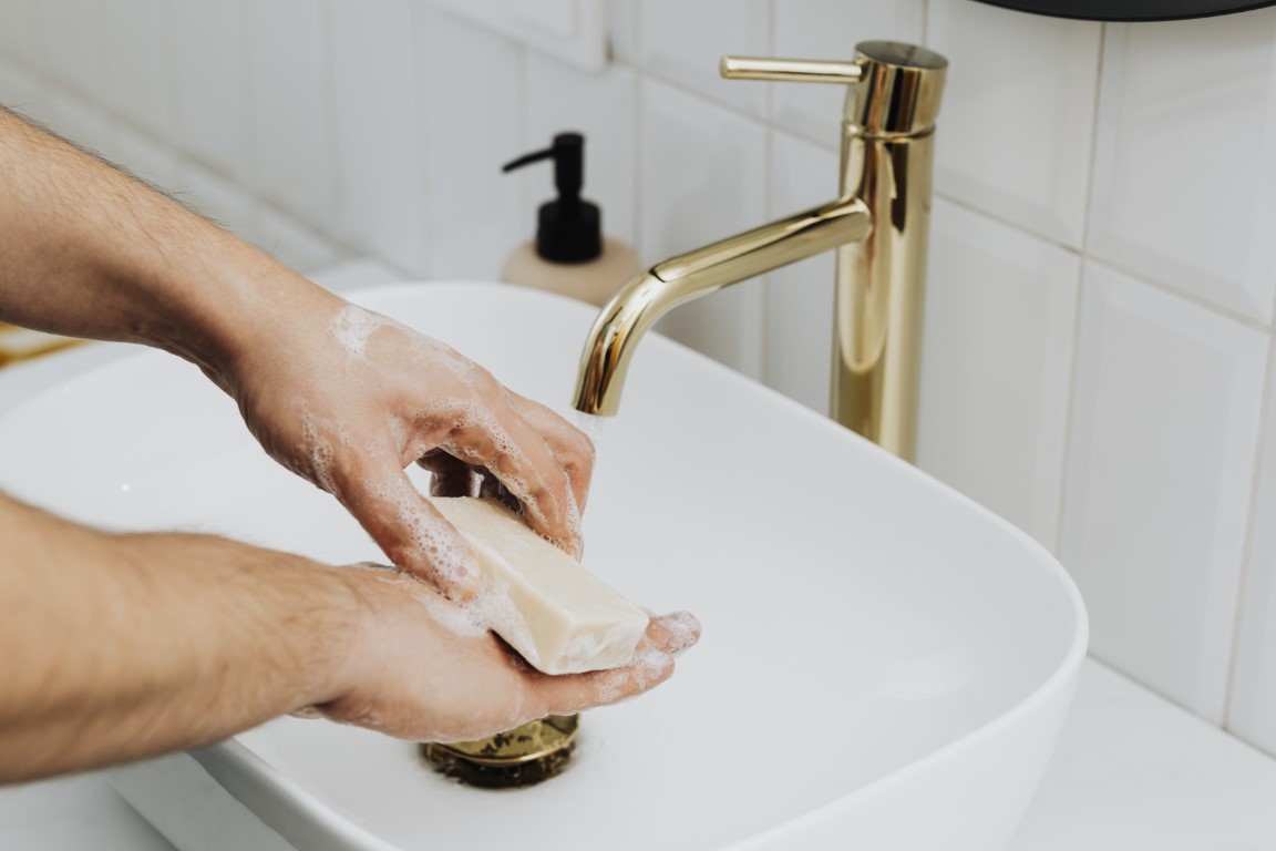 Zwei Hände die sich mit einem Stück Seife an einem hochwertig aussehendem Waschbecken waschen.
