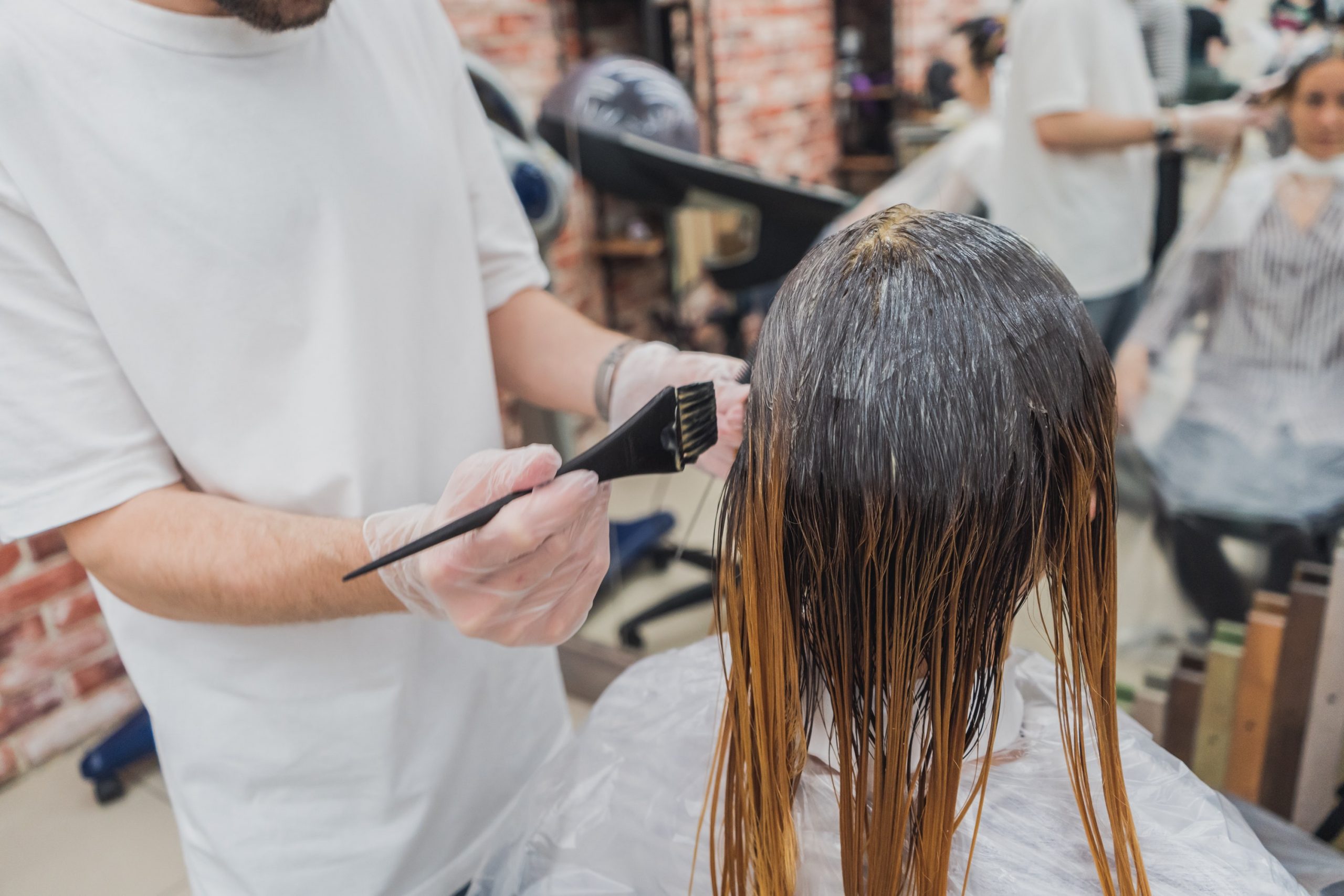 Eine langhaarige Frau sitzt im Friseursalon während die Frisörin mit einem Pinsel eine permanente Haarfarbe aufträgt.